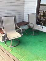 Two patio swivel chairs and small side table on green outdoor carpet