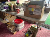 Side view of the white plastic folding-legged table showing boxes and various items on top and around it.