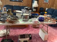 Full view of the large plastic folding leg table with various kitchen items placed on top, showing the table's size and structure in a living room setting.