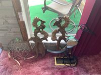 Two plaster calypso dancer sculptures, metal dream catcher, and metal bird art seen on carpet near a window and chair.