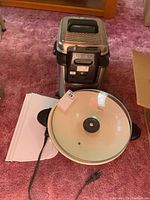 Oster electric wok and T-fal deep fryer placed on carpet floor, showing front and top views.
