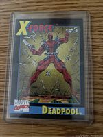 Front of Deadpool rookie card showing Deadpool with pistols and bullet holes on gold background.