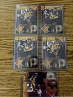Top view of 5 Kobe Bryant basketball cards in protective plastic sleeves laid out on wood surface.