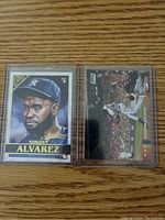 Two Yordan Alvarez MLB rookie baseball cards in plastic sleeves on wooden surface.