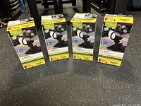 Four boxed Better Homes and Gardens QuickFit LED spotlights standing upright on a floor.