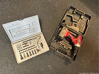 Photo of a red cordless drill in a black plastic carrying case with various drill bits and accessories.