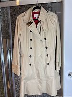 Beige trenchcoat hanging, showing full front double-breasted button closure and collar