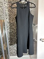 Full view of black sleeveless dress hanging on hanger, showing shape and design.