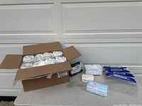 Wide view of all safety equipment including opened box with individually wrapped white N95 masks, boxes of surgical masks, multiple clear plastic face shields, and a white CO2 monitor device.