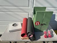 Full lot on table showing three yoga mats, two pink dumbbells in plastic, and green body fat caliper.