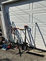 Full view of garden and cleaning tools including rakes, shovels, brooms, and hand tools leaning against garage door