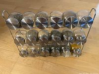 Front view of metal spice rack displaying all 15 labeled glass spice jars filled with various spices.