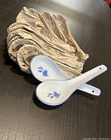 Two ceramic Chinese soup spoons with blue floral designs, resting on a dark surface with crumpled paper beneath them.
