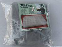 Photo of air mattress in original plastic packaging with instructional label in French showing the mattress image and usage information.