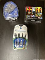 Three cable packages arranged on a black surface: a clamshell ZOOM USB adapter, a sealed 6ft HDMI value pack with two HDMI cables and cleaner solution, and a 9-in-1 USB 2.0 cable kit with multiple connectors in sealed packaging.