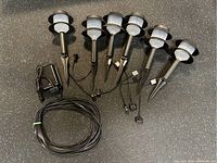 Six black outdoor pathway lights with white diffuser covers and stakes, and coiled black wire.