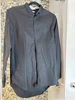 Front view of a black long-sleeve men's dress shirt laid flat, showing buttons and collar.