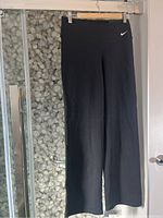 Full front view of black Nike yoga pants hanging on a wooden hanger, showing Nike swoosh logo near waistband.