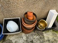 Overview of various planters including stacked terracotta pots, white hanging planter, and black square plastic planters on the ground outside.