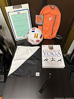 Photo showing a white and black lululemon drawstring bag, a multi-flag soccer ball, orange sports backpack, coaching clipboard, yoga book, and black flashlight-like device.