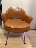 Front view of smooth brown faux leather accent chair with rounded seat and back, supported on four chrome metal legs.