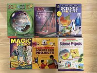 Top view of six science project and magic science books aligned on a wooden surface.