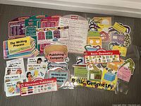 Top-down view of various educational posters and cutouts for classroom use including writing process, parts of speech, publishing and geometry themes.
