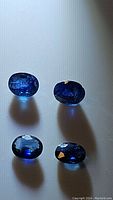 Four oval cut blue sapphires arranged on a white surface under diffused light showing their clarity and color.