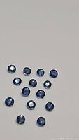Photo showing 14 round cut, natural denim blue sapphires arranged on a white background, illustrating the size, cut and color of the stones.