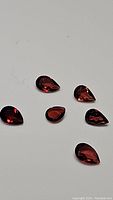 Photo of six pear-shaped garnet gemstones with deep red fancy color on a white background.