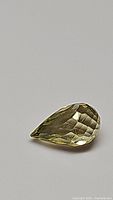 Clear image showing one pear-shaped lemon citrine gemstone with fancy briolette cut facets on a gray background.