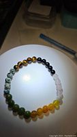 Round gemstone bead bracelet featuring multiple stone types arranged in color sections on a white surface.