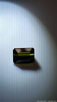 Rectangular emerald-cut natural forest green tourmaline on white background under direct light.