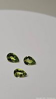Photo of three natural pear cut apple green Peridot gemstones on white background showing color and clarity