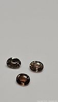 Three oval-shaped natural champagne zircon gemstones placed on a light background, showing their color and luster.