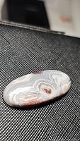 Oval cabochon white crazy lace agate gemstone featuring intricate banding and color variation including white, brown, and red.