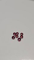 Seven natural deep raspberry pink sapphire round cabochon gemstones on plain white background showing size and color.