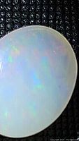 Close-up of natural oval Ethiopian opal cabochon showing multi-colored fire and sheen on a textured black background.