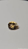 Close-up image of pear-shaped golden citrine gemstone on a neutral background showing facets and clarity.