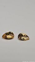 Two pear cut natural golden citrine gemstones displayed side by side on a plain background, showing their matching color and size.
