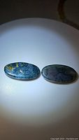 Pair of oval cabochon moss agate gemstones under light showing unique moss-like inclusions and color variations.