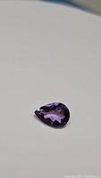 Close-up image of a pear-shaped natural purple amethyst gemstone showing facets and color.