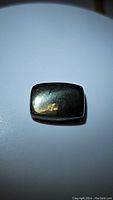 Image showing natural golden pyrite cabochon with reflective polished surface and cushion cut shape on white background.