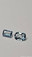 Pair of natural sky blue topaz gemstones, emerald cut and long cushion checkerboard cut, displayed on a neutral background.