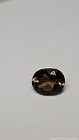 Photo showing the natural oval cut Smokey Quartz from an angled top view, highlighting its color and faceting.