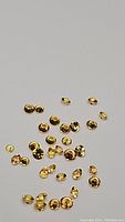 Top view of loose tiny oval and round faceted yellow sapphires scattered on white background, showing their yellow hue and size