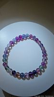 Top view of the rainbow fluorite bead bracelet with beads in shades of purple, green, blue, and clear on a stretchy cord.