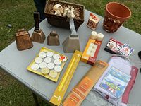 Full lot showing bells, planter with animals, candles, and containers arranged on table outdoors.