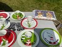 Christmas dishware set on outdoor folding table including holiday plates, mugs, and silverware.