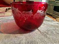 Side view of the red glass bowl showing white etched holly leaf pattern.